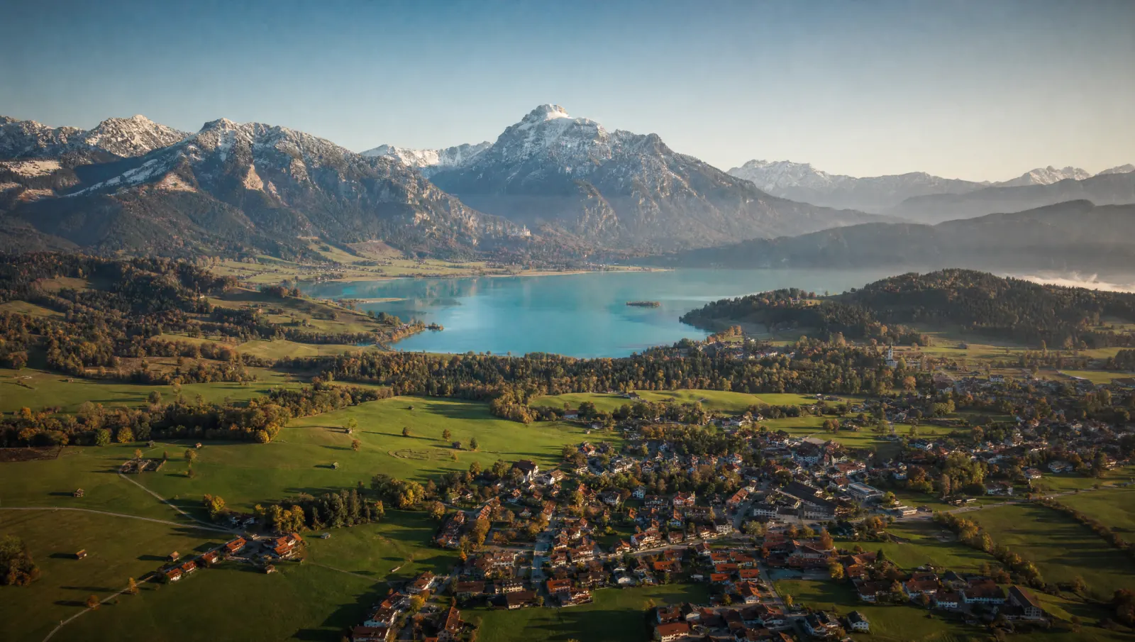Luftbild des bayerischen Oberlands mit See, Wiesen und den Alpen im Hintergrund